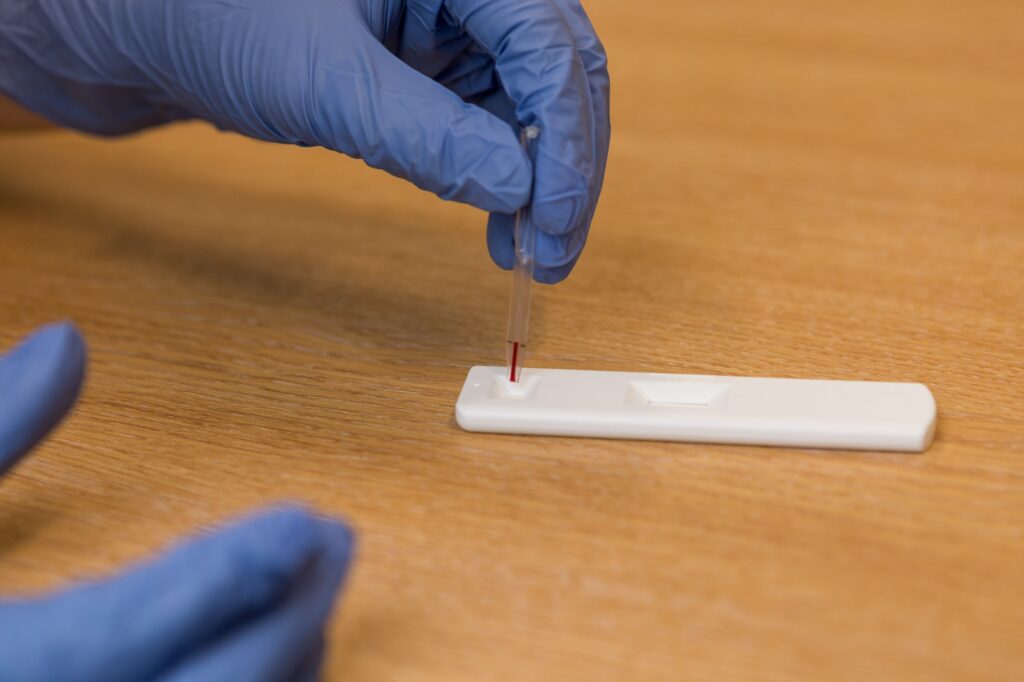 someone adding blood sample to AbC-19 COVID-19 rapid antibody test